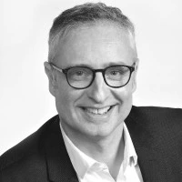 Portrait en noir et blanc d'un homme souriant avec des lunettes.