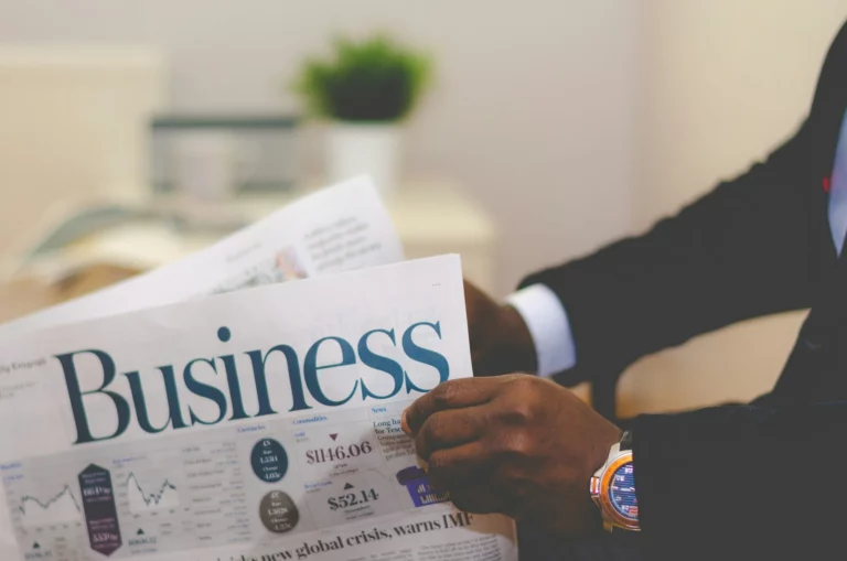 Un homme en costume lisant un journal financier avec le titre "Business" en gros caractères.